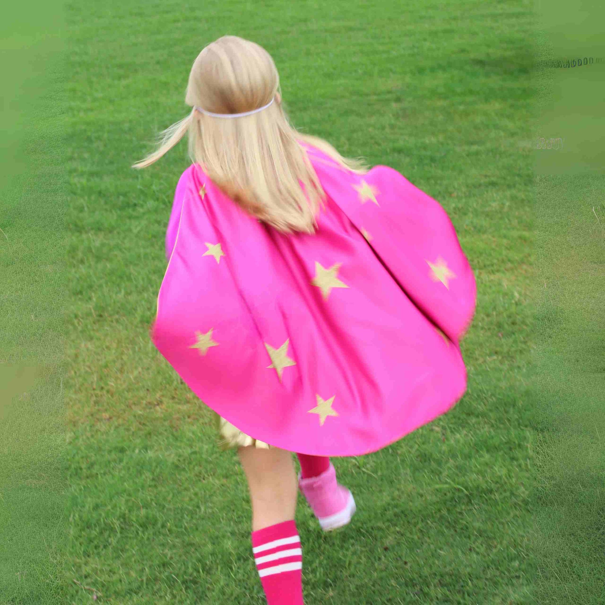 a little girl in a pink cape walking across a field